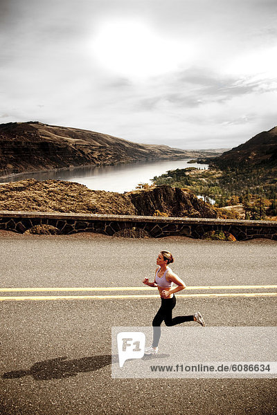 An athletic woman jogging along a deserted road on a beautiful fall day with the Columbia River Gorge in the distance.