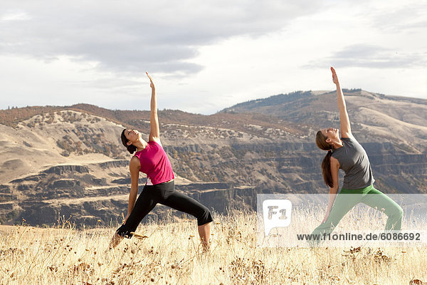 Two females practicing yoga in the outdoors with the Columbia River Gorge in the distance.