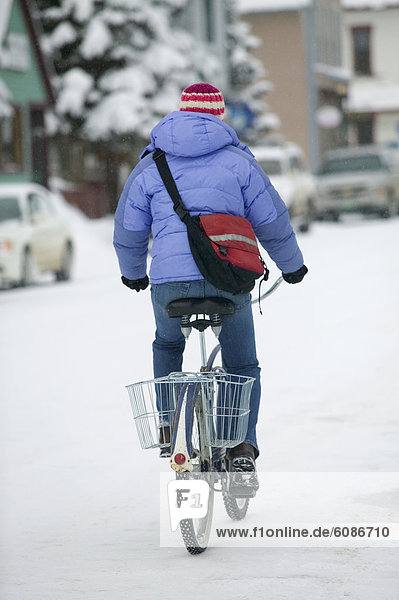 Woman riding a bike down snow covered Elk Avenue  Crested Butte  Colorado.