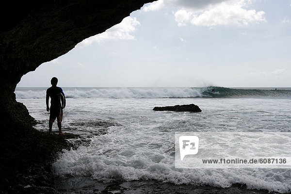 A surfer looks on as another surfer surfs a wave at Balangan  Bali  Indonesia.