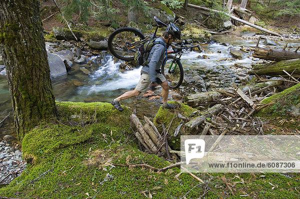 A man carries his mountain bike over a washed out portion of a trail in northern Idaho.