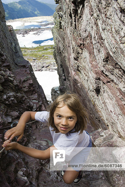 A young girl makes her way up a narrow slot in a cliff while hiking in Glacier National Park  Montana.