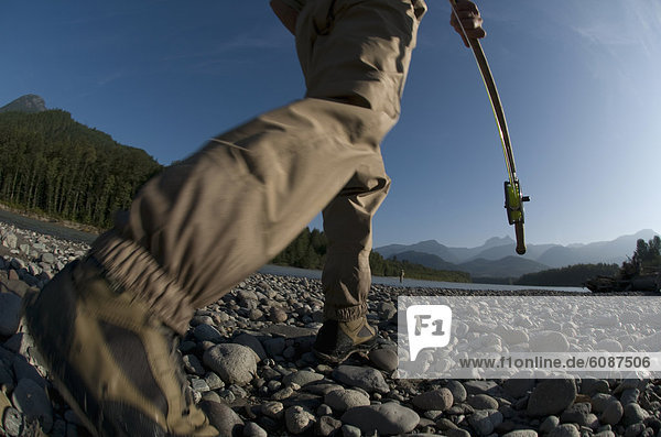 A man holding a fishing rod walks to the river to go fly fishing in Squamish  Brithish Columbia. (motion blur)