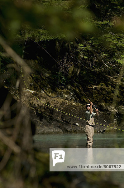 A man casts in a river wearing waders while fly fishing in Squamish  British Columbia.