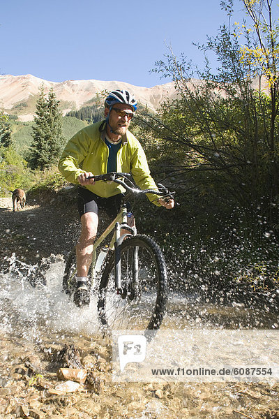 A man mountain biking across a mountain creek outside of Ophir  Colorado.