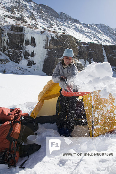 A woman shovelling snow away from her tent while winter camping in the Sangre De Cristo Mountains  Colorado.