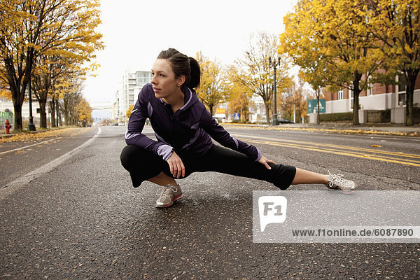 An athletic female in a purple jacket stretching along a deserted street in Portland  Oregon.