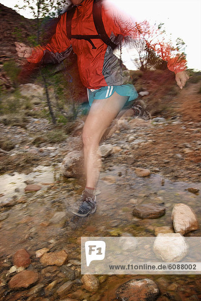 A woman trail running through a rocky stream in Nevada.