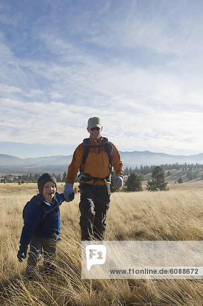 A young boy and his father hike an open field.