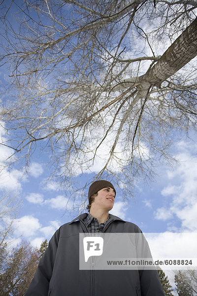 Portrait of a teenage male standing underneath a tree and blue sky.