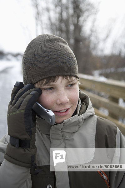 A young boy in winter clothing talks on a cell phone.