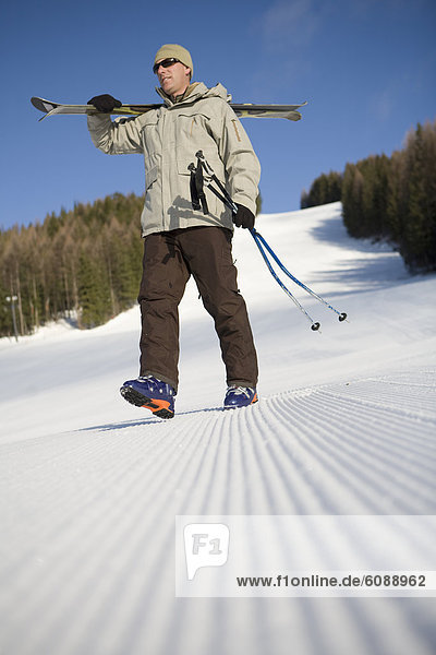 Male skier walk across freshly groomed ski slope.
