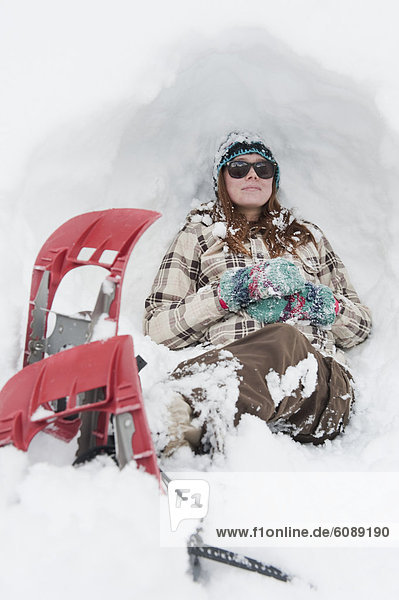 Young woman rests in the snow with snowshoes on in Milcreek Canyon  Salt Lake City  Utah.