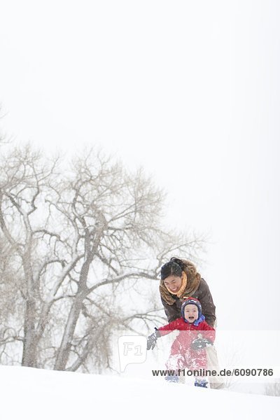 A two year old boy plays in a snowy field during a snowstorm in a red snowsuit with his mother in a park  Fort Collins  Colorado.