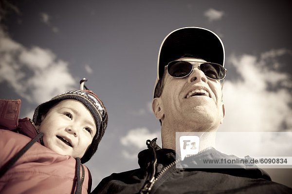A two year old boy is held by his grandfather  an active senior  on a blue sky day in the mountains of Colorado.