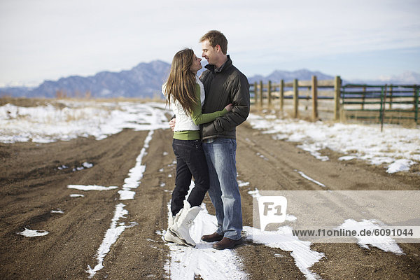 Couple looking at each other almost kissing by the snow in a field.