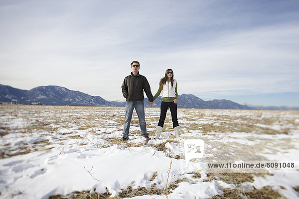 Couple holding hands and looking away in a snowy  open field.