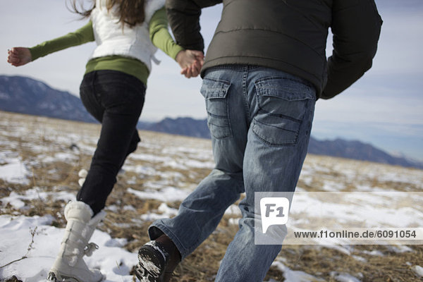 Couple holding hands and running by the snow in a field.