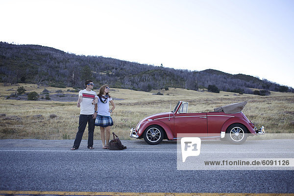 Young couple stand on the road by their broken retro car and try to hitchhike.