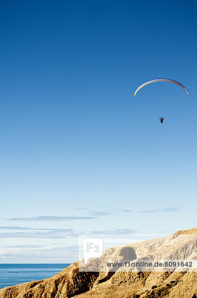 On a bright blue sky a hang glider flies above the cliffs in Torrey Pines in La Jolla  California.