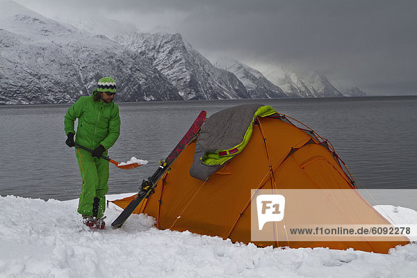Norwegen  Skifahrer beim Schneeräumen mit Schaufel am Zelt