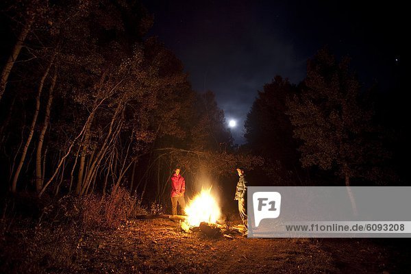Two males standing around a fire while camping in Colorado.