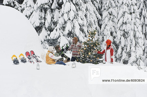 Österreich  Salzburg  Männer und Frauen im Winter am Weihnachtsbaum sitzend