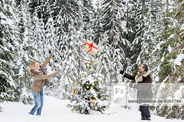 Österreich  Salzburger Land  Paar spielt mit Weihnachtsgeschenk im Schnee  lächelnd