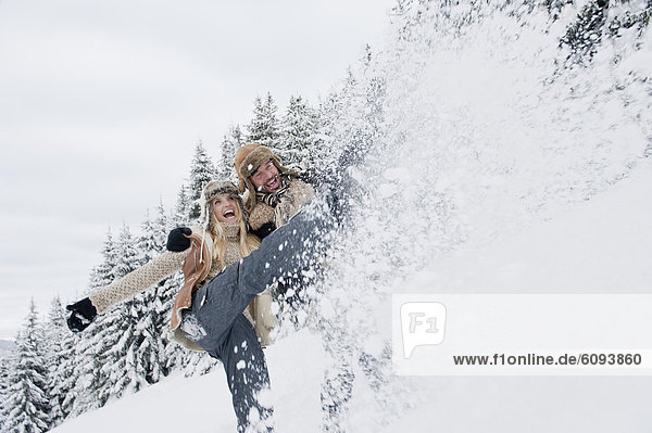 Österreich  Salzburger Land  Paar plätschernder Schnee in verschneiter Landschaft lächelnd