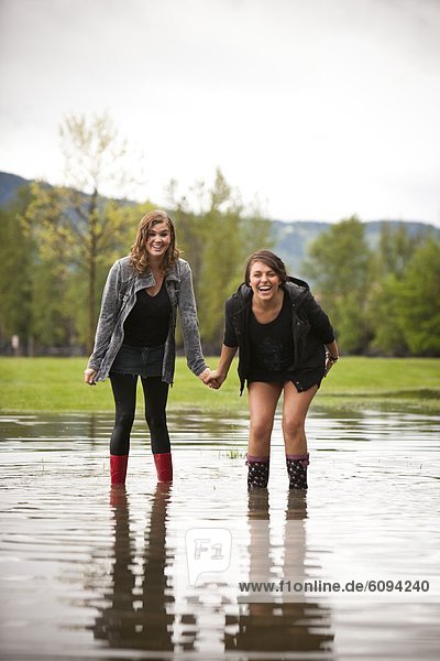 Two young women hold hands after a water fight in a large puddle.