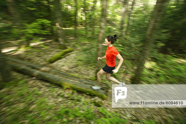 Woman trail running in a lush green forest.