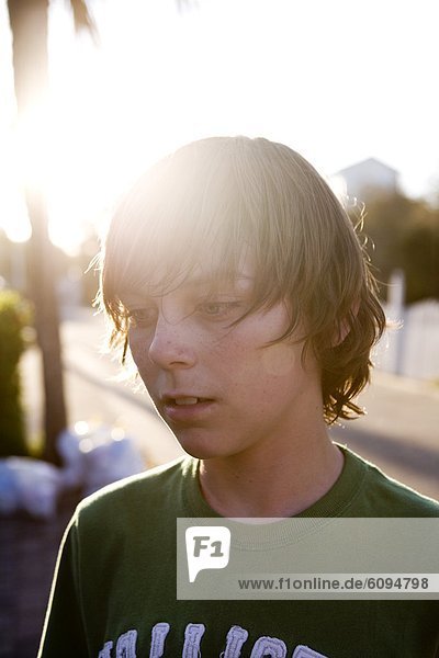 A teen boy is staring with the sun shining behind him.