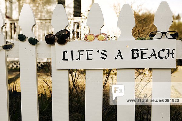 'A picket fence is covered with sunglasses and has a sign that reads ''life's a beach''.'