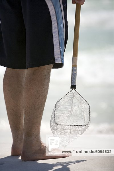 A man holds onto a bait net at the shoreline.