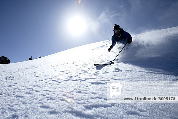 Low angle perspective of one man telemark skiing on a blue sky day.