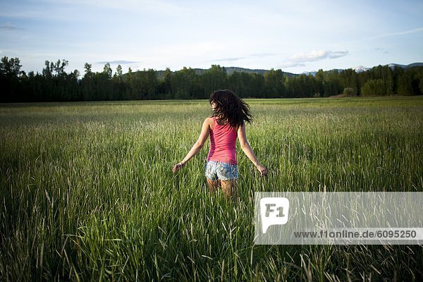 A girl twirls through tall grass on a sunny day in Idaho.