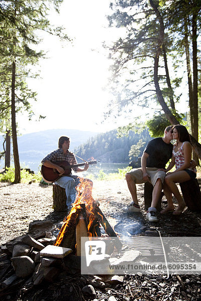 Young adults camping sit around a fire next to a lake in Idaho.