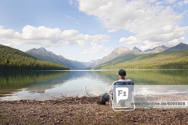 An older man sits next to a lake in Glacier National Park  MT