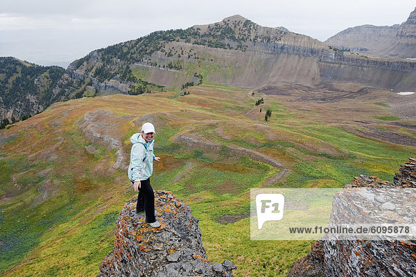 A young woman stands on a rock overlooking a colorful field on Mt. Timpanogos  near Pleasant Grove  UT.