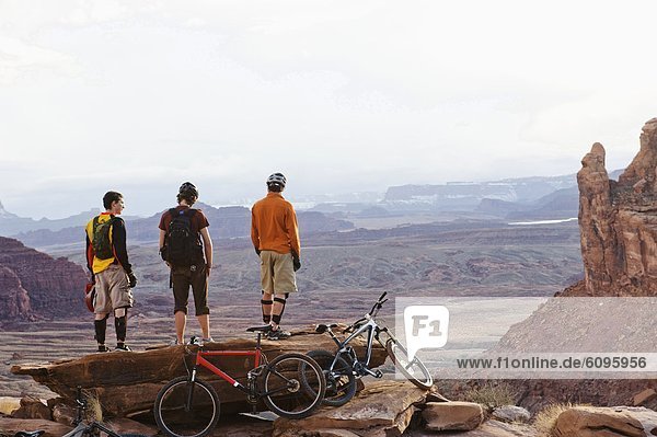 Three young men overlook a canyon after biking up the Amasa Back Trail  Moab  UT.