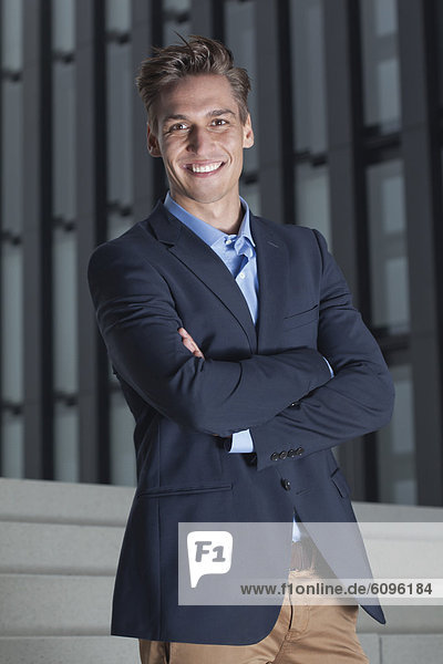 Germany  North-Rhine-Westphalica  Duesseldorf  Young businessman standing with arms crossed  smiling  portrait