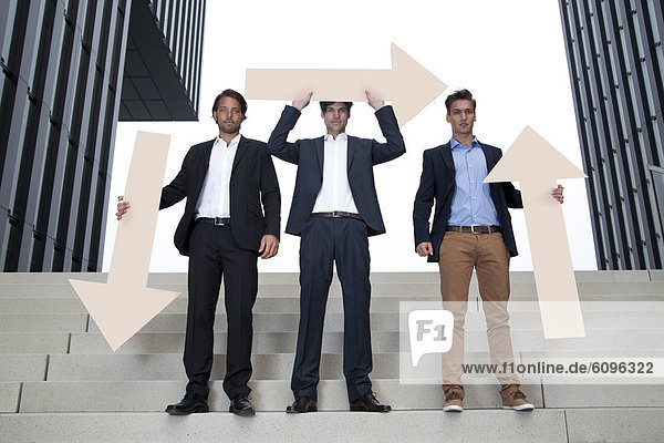 Germany  North Rhine Westphalia  Duesseldorf  Young businessmen standing on steps with arrows in different directions
