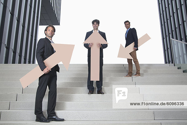 Germany  North Rhine Westphalia  Duesseldorf  Young businessmen standing on steps with arrows in different directions