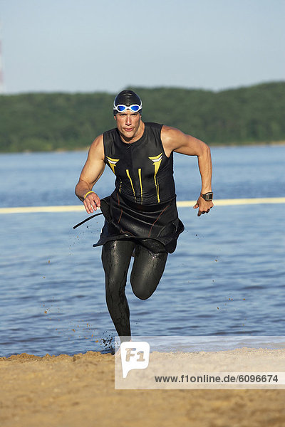 A male athelete running out of the water while training for a triathlon.