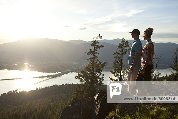 Two young adults talk at the edge of a cliff enjoying the view of the lake.