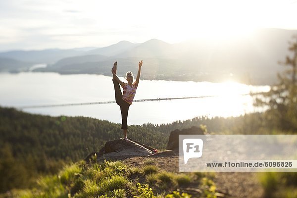Young woman doing yoga at the top of a mountain overlooking a small town and large lake.
