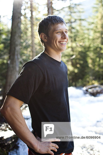 A young man smiles while standing next to a raging river in Idaho.