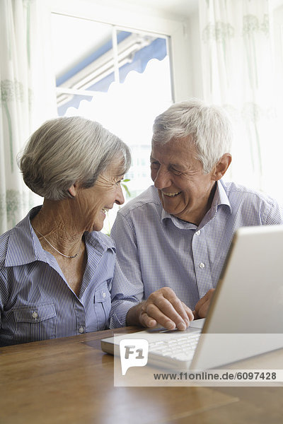 Germany  Bavaria  Senior couple using laptop at home  smiling