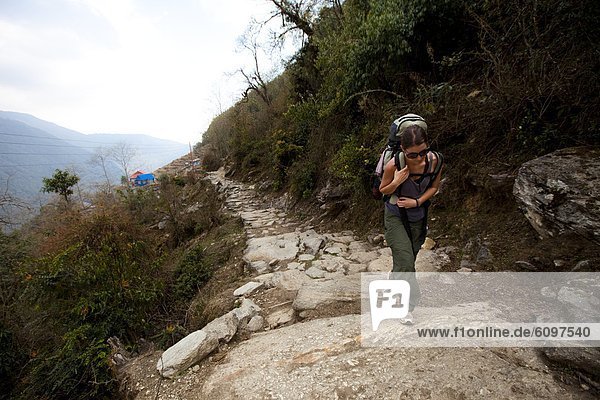 A female trekker shoulders her rucksack uphill in Nepal.