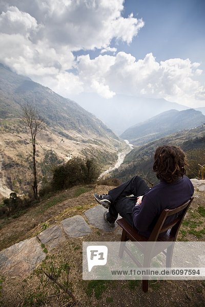 A trekker rests in a wooden chair to study the weather in a valley below.